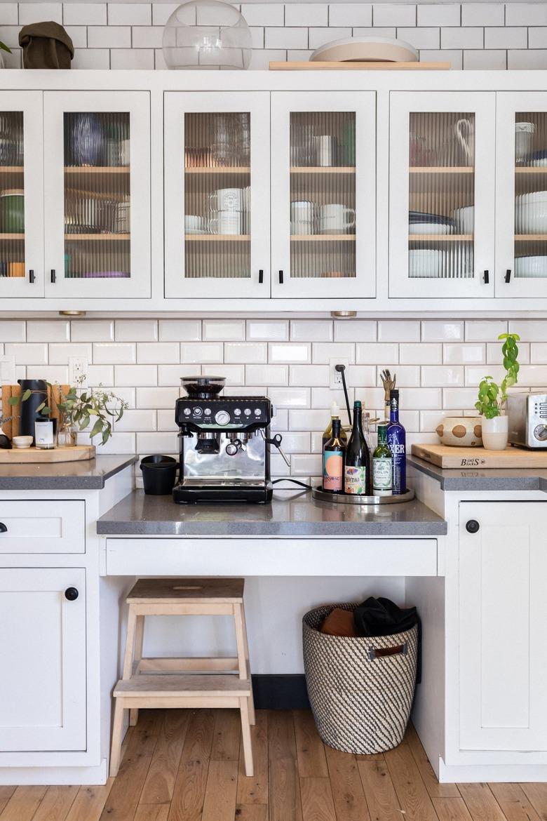 Kitchen with white cabinets, subway tile, coffee maker, stool.