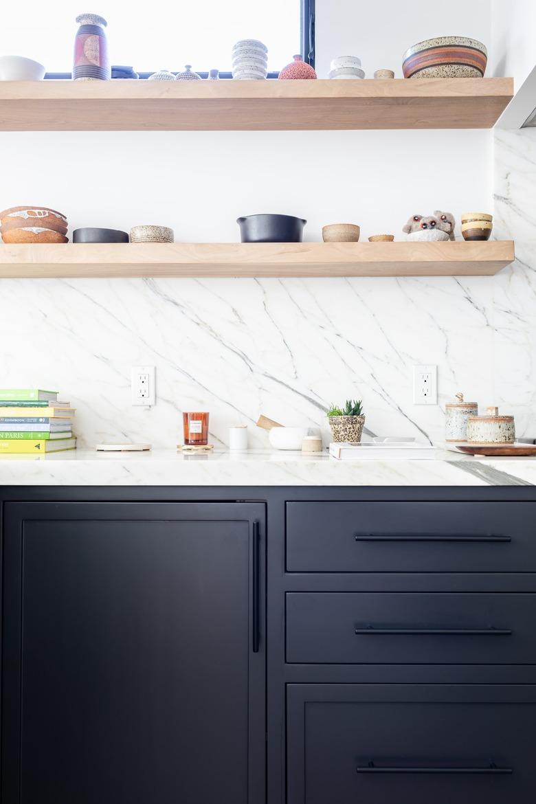 White walled kitchen with dark gray cabinets and wood shelving with pottery