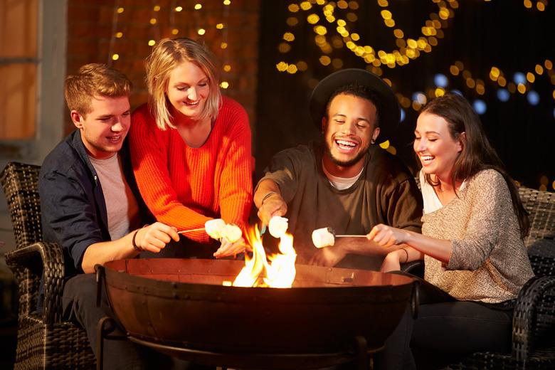 Group of friends toasting marshmallows by firepit.