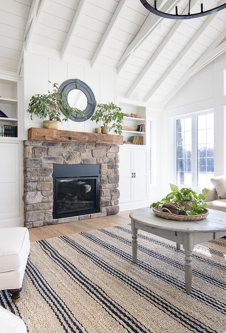 white living room with coastal fireplace made of stone with porthole mirror above