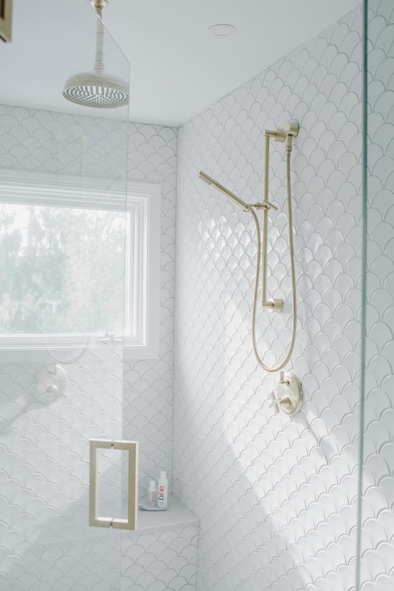 Coastal shower with white fish-scale tiles and gold fixtures