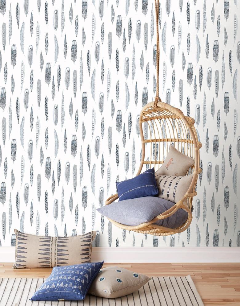 rattan hanging chair against blue and white feather coastal wallpaper