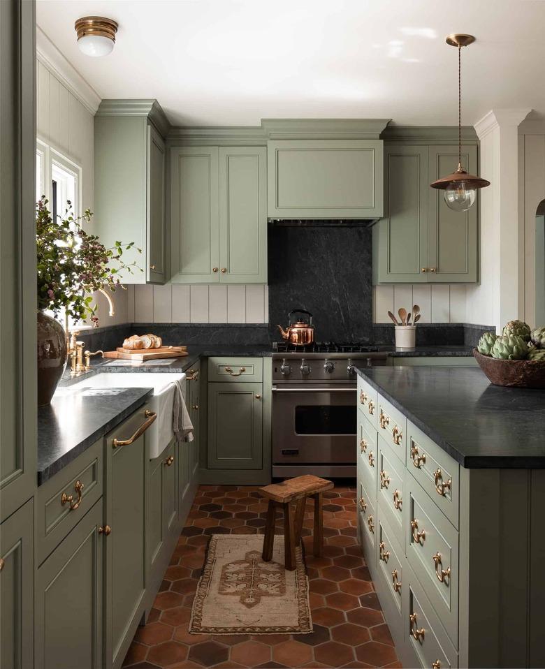 Kitchen with green cabinets, black countertop, and terra cotta tile floor