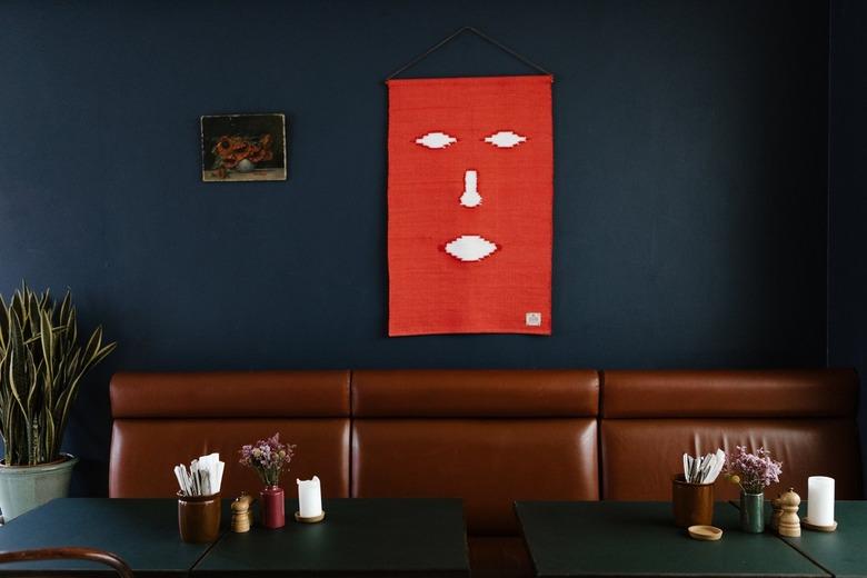 Brown leather booth and green table against blue wall with eclectic art and plant