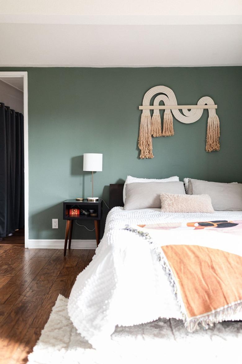 Green walled bedroom with wood floors and neutral textiles