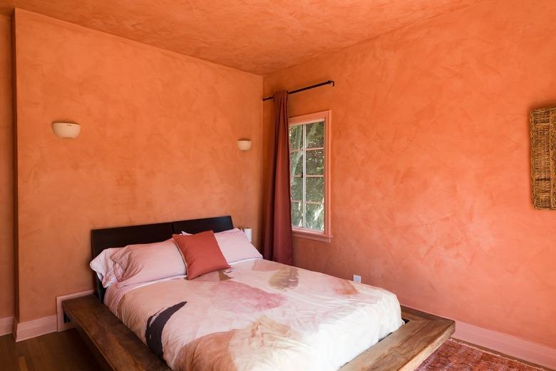 Bedroom with orange walls, white wall sconces, orange begging and pillows, orange curtains, and dark wood floor.