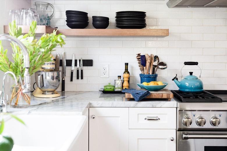 white kitchen with pale gray stone countertops and wooden floating shelf