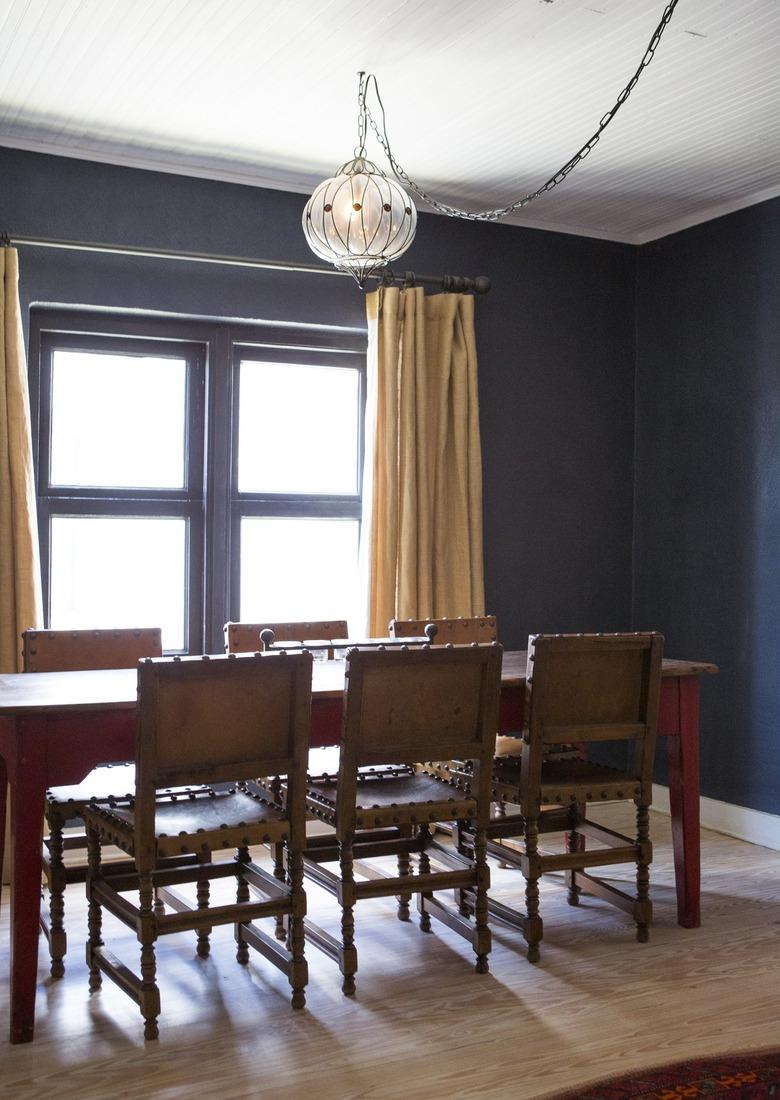 A dark blue walled dining room with wood dining room and globe pendant light