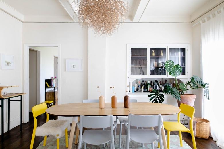 Wood dining table with yellow and white chairs and a contemporary chandelier