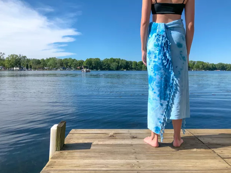 Tie-dye towel wrapped around woman looking out on a lake