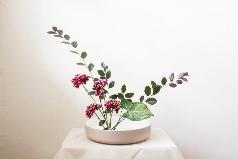 White Ikebana vase with pink flowers and green leaves on a white table