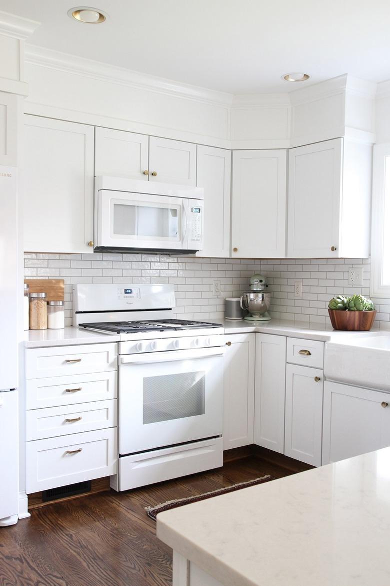 Recessed kitchen ceiling lights in all-white kitchen with wood flooring