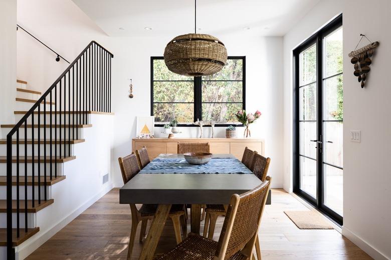 Dining room with white walls and wood floors with large windows and a staircase