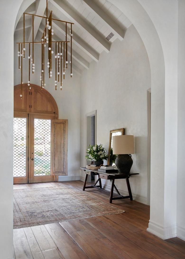 Entryway with rug, console table, lamp, wood floors, double french doors, modern chandelier.