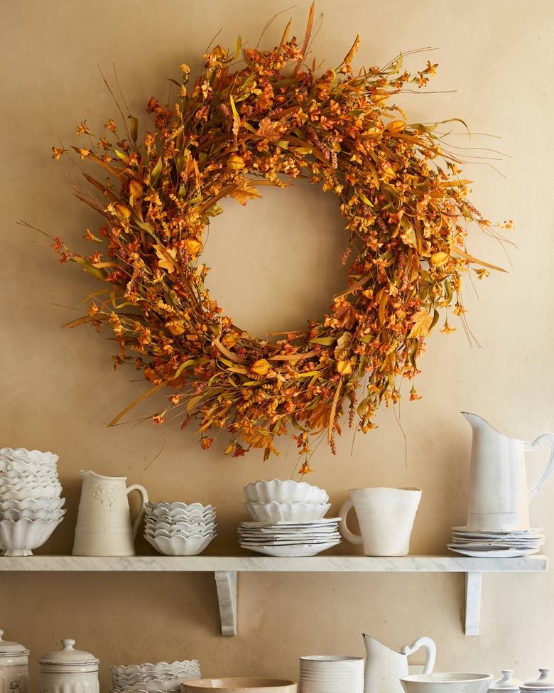 fall wreath made with forsythia hanging above a shelf with dishes