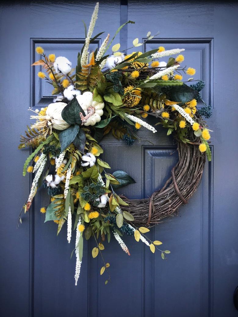 fall wreath made with grapevine, white pumpkins, yellow flowers, and greens