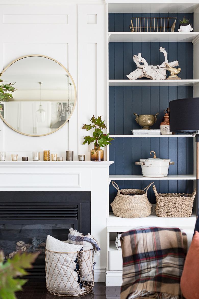 Living room with built in shelves, round mirror, baskets, plaid throw, fireplace.