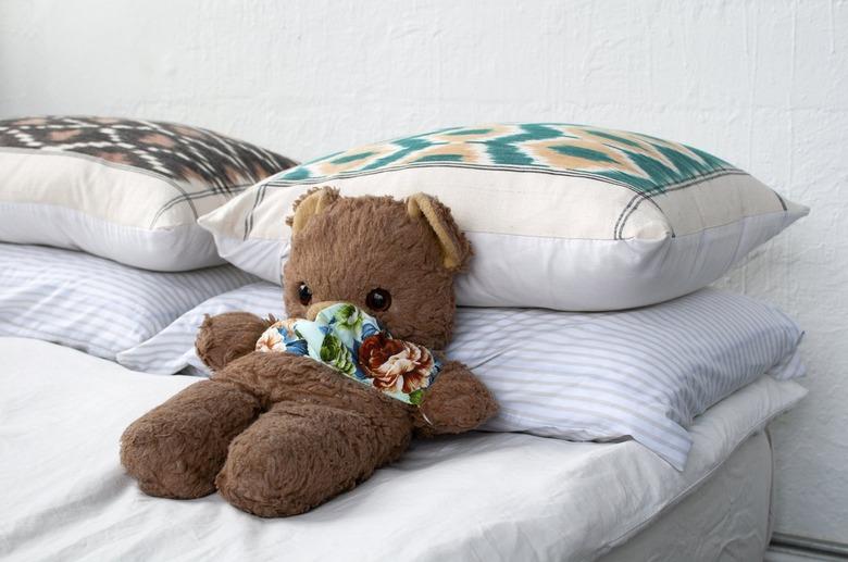 A brown teddy bear on a bed with white bedding and multicolored pillows