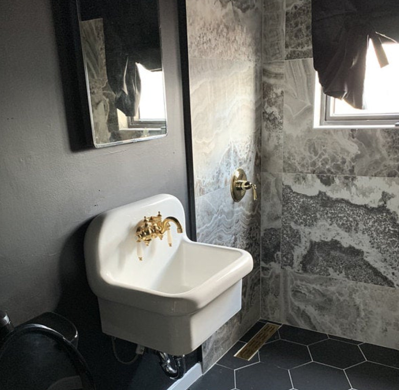 French country bathroom sink in marble and stone bathroom with open shower, wall mounted sink, brass faucet.