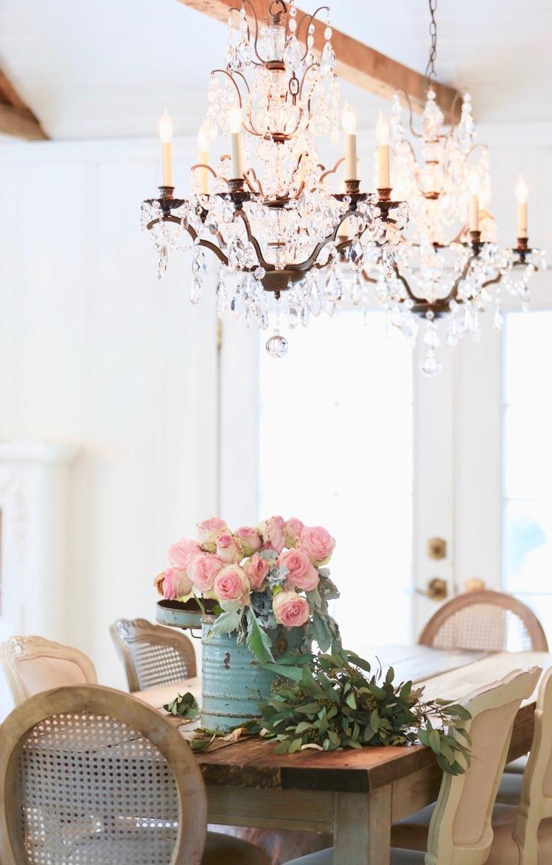 French country dining room with crystal chandeliers above rustic table