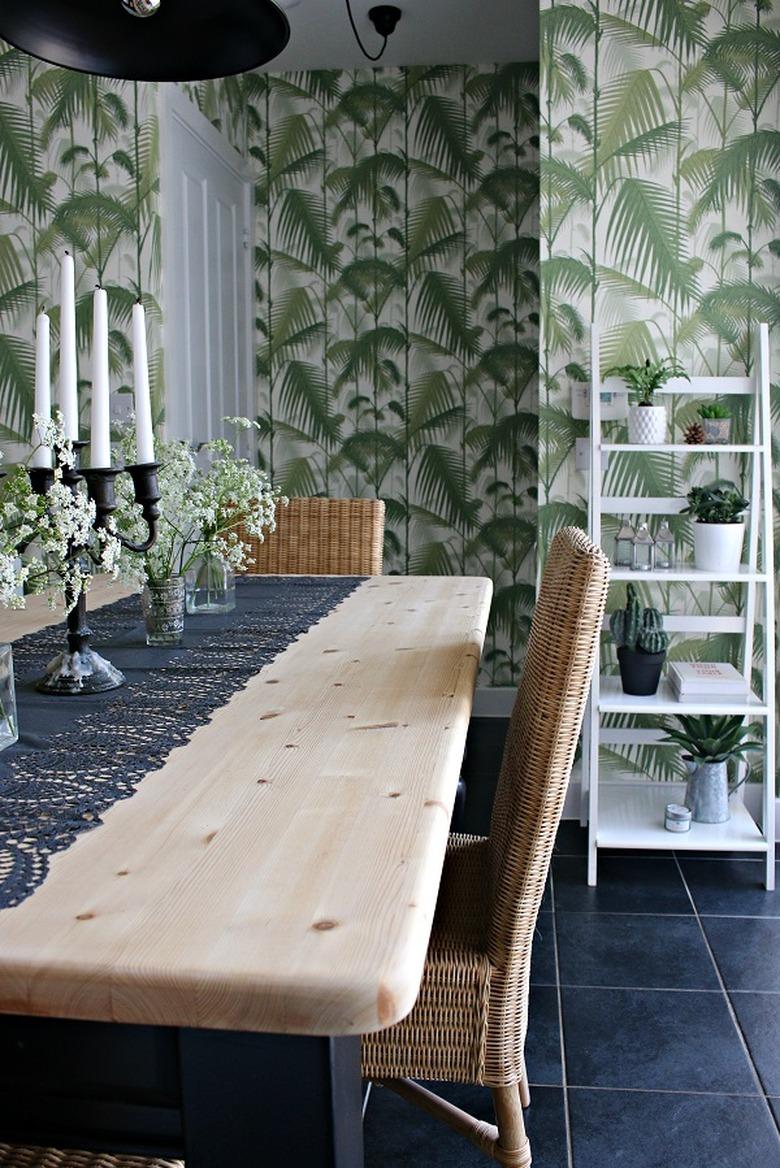 Green boho room with natural wood table and palm leaf wallpaper