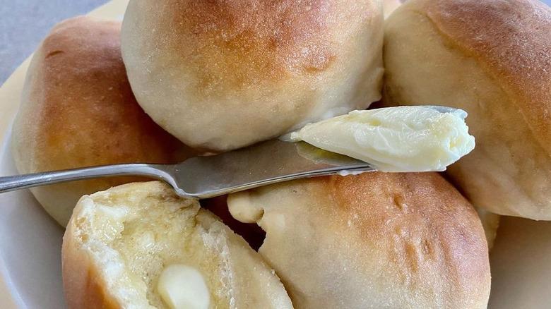 A plate of Hawaiian rolls and a knife with butter