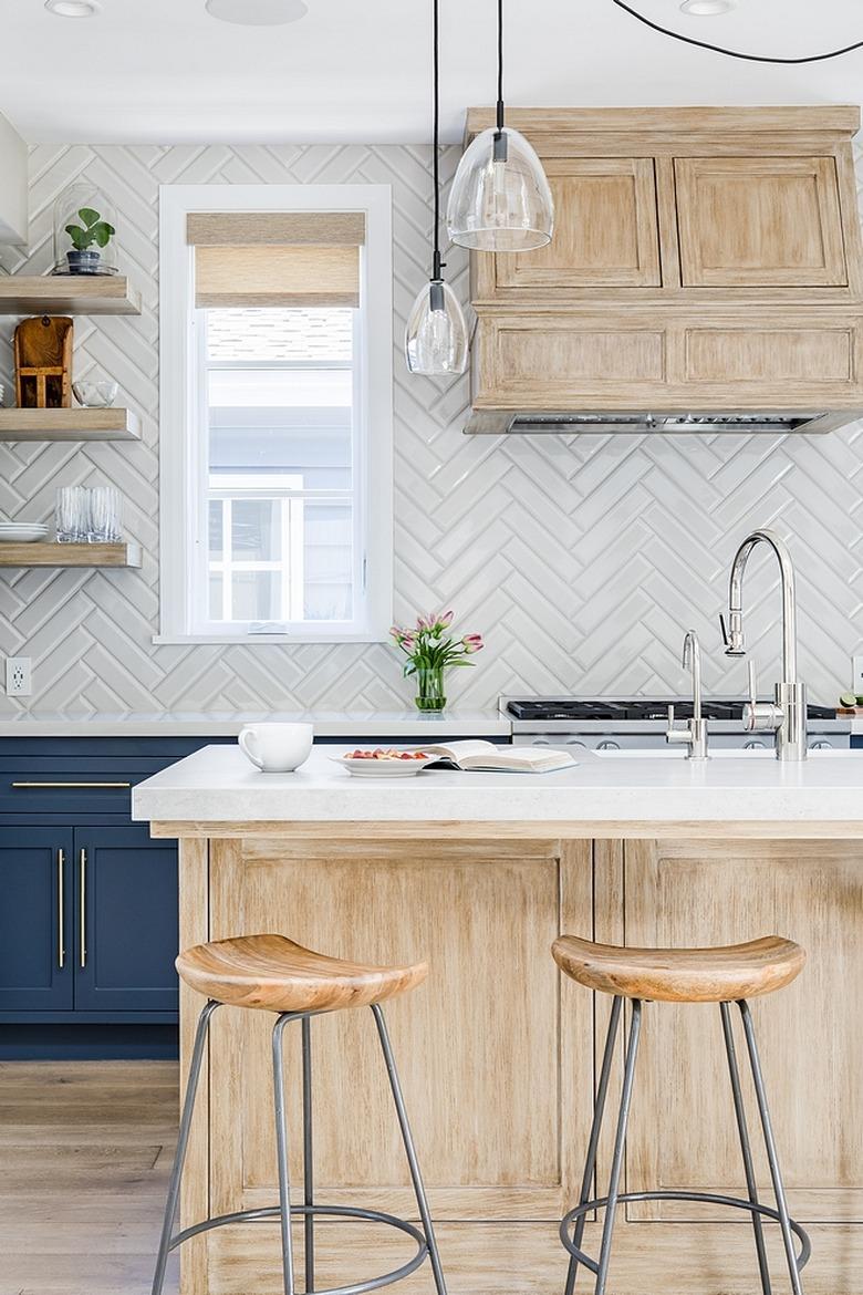 White herringbone backsplash with light wood island and navy blue cabinets