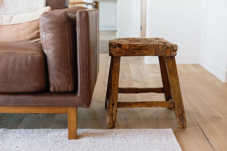 A small wooden stool next to a brown leather couch.