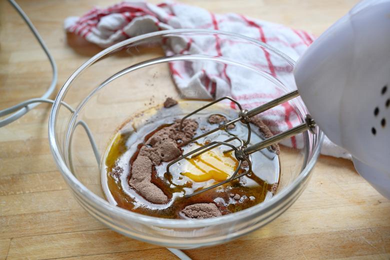 electric mixer in a glass bowl with cake dough of egg, cocoa and flour on a wooden table with a kitchen towel, baking concept