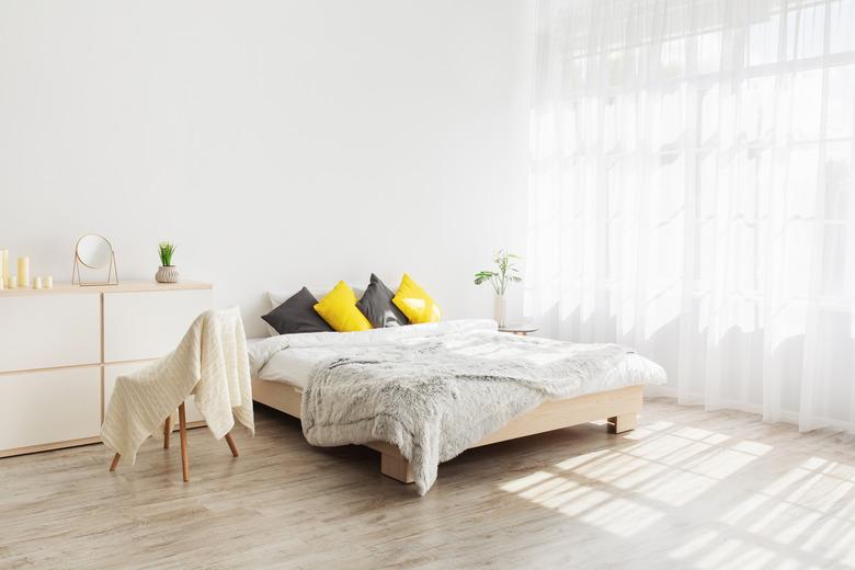 Cozy, feminine bedroom with throw pillows and plants at white blank wall