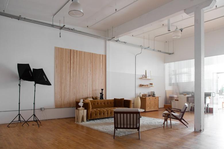 Minimalist living room with hardwood floor, white shag rug, brown velvet couch, wood slat accent wall, photography lamps.