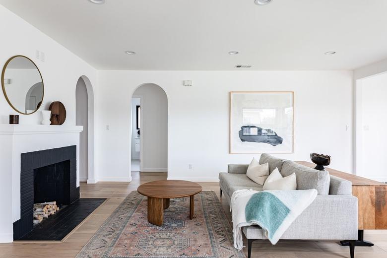 Contemporary living room with black fireplace, decorative logs, green couch, and archway leading to hall.