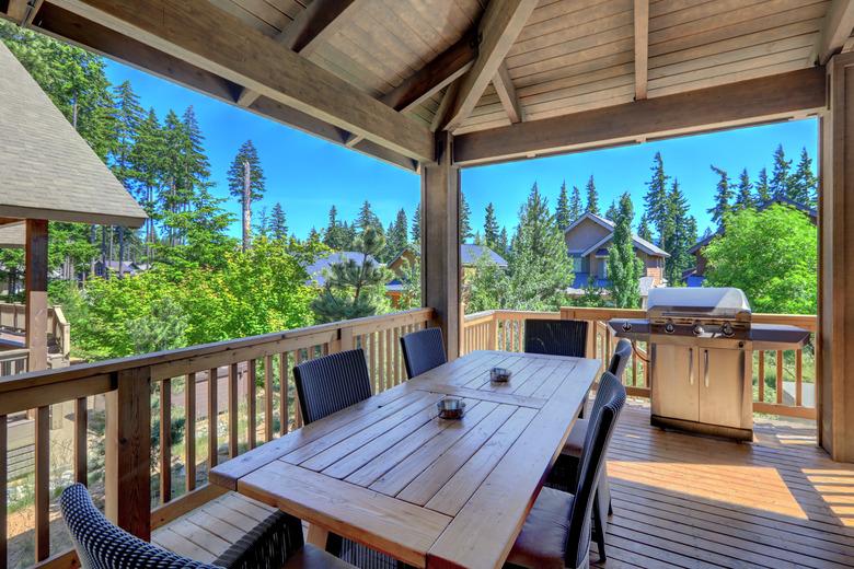 Beautiful covered deck with large luxury dining room table with grill and railings.