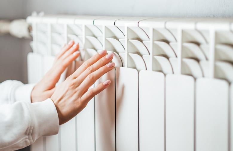 Woman warms up hands over heater.