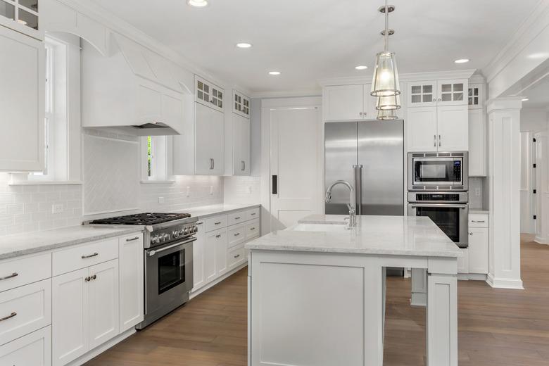 beautiful white kitchen in new luxury home with island, pendant lights, and hardwood floors. Features stainless steel appliances and farmhouse style sink