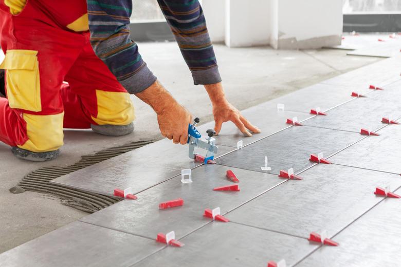 Ceramic Tiles. Tiler placing ceramic wall tile in position over adhesive with lash tile leveling system