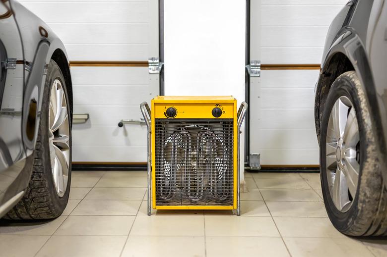 Big heavy industrial electric fan heater in double car garage interior. Two vehicles parked for winter storage in dry warm heating parking for cold winter season.