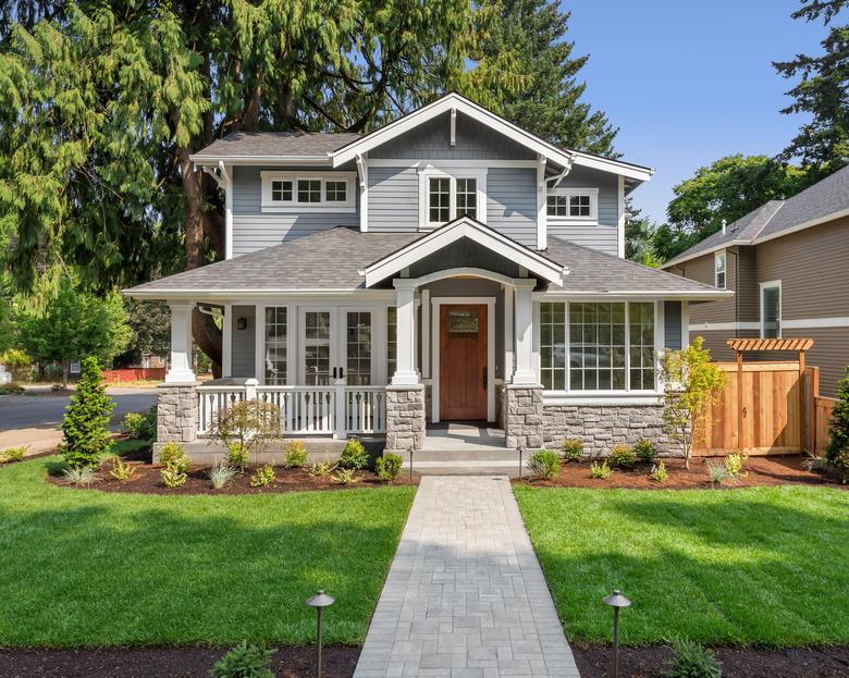 Beautiful luxury home exterior on bright sunny day with green grass and blue sky. Features walkway, covered porch, and stately gables and columns.