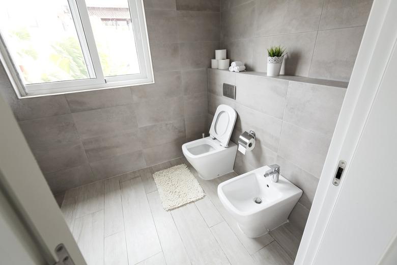 Half-open door to luxury bathroom with white ceramic bidet and toilet