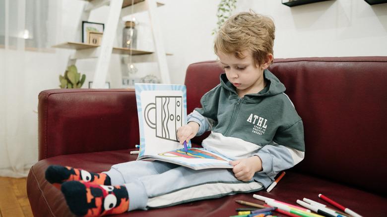 Boy sitting on couch drawing or coloring with markers.