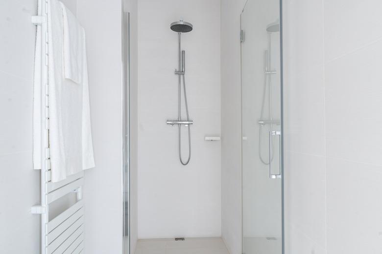 White bathroom shower with a glass reflection and white towel hanging on a wall