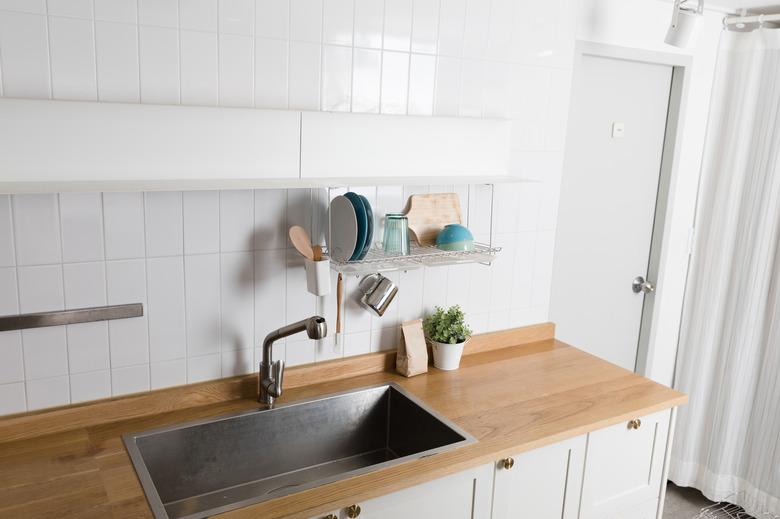 Clean dishes drying on metal dish rack on light background. Kitchen utensils and dishware on wooden shelf. Kitchen interior background.Text space.