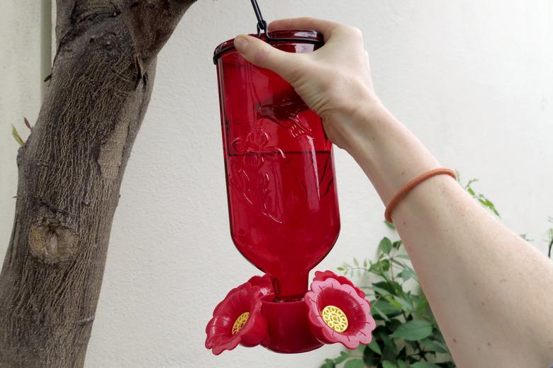 Hand moving a hummingbird feeder.