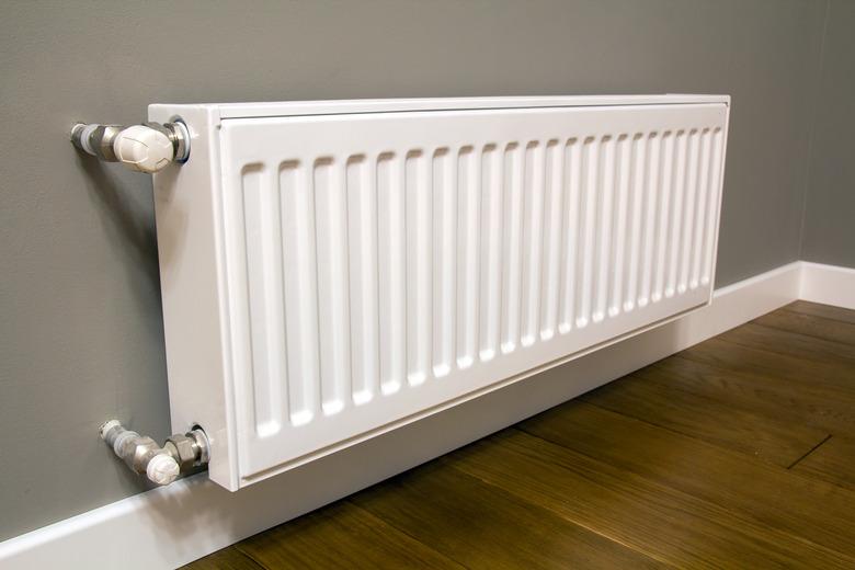 White metal heating radiator mounted on gray wall inside a room.