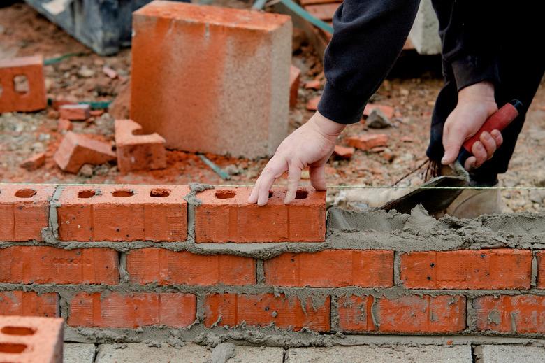 Bricklayer laying bricks on mortar on new residential house construction site