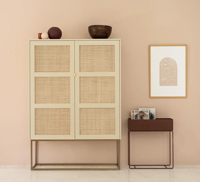 cane dresser with small side table and framed artwork nearby