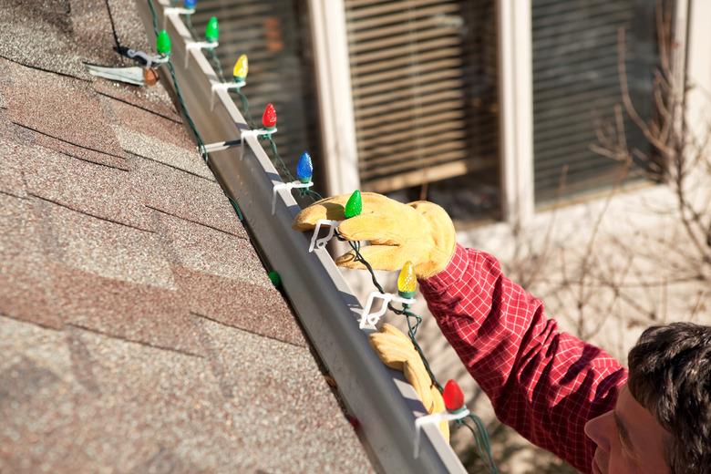 Man using clips to install LED Christmas lights on gutter.