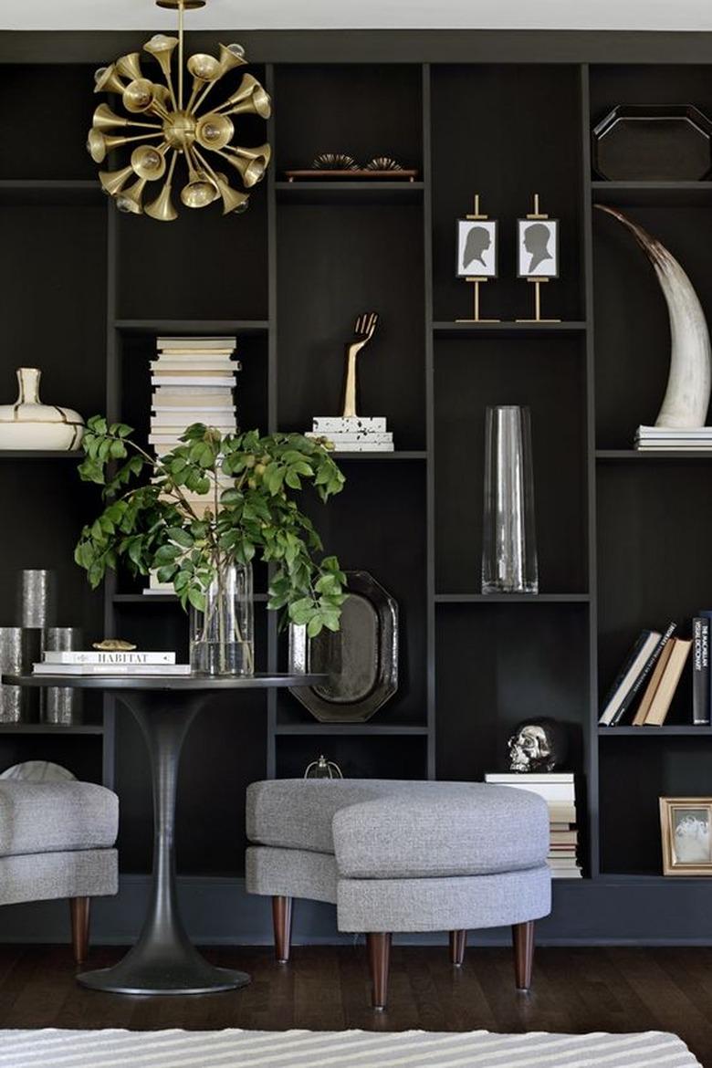 How To Organize a Bookshelf in room with Dark gray built in shelving, art, plant, curved gray benches, bistro table, modern pendant lamp, books.