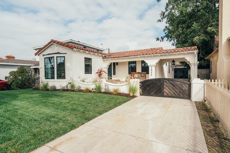 White home with Spanish-style roof, green grass lawn, concrete driveway with wooden gate