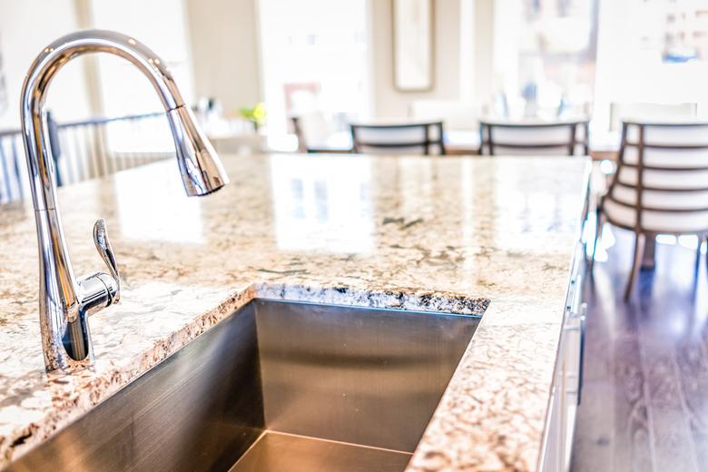 New modern faucet and kitchen room sink closeup with island and granite countertops in model house, home, apartment